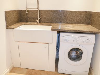 A utility area with a white sink and faucet next to a front-loading washing machine at 1 Orchard Cottages in Salcombe