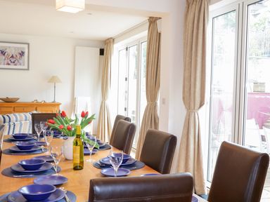 A dining room with a wooden table set with blue plates and bowls and a vase of red tulips at 1 Orchard Cottages in Salcombe