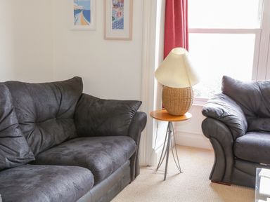 A living room with two dark sofas a small side table with a lamp and framed pictures on the wall at 1 Orchard Cottages Salcombe