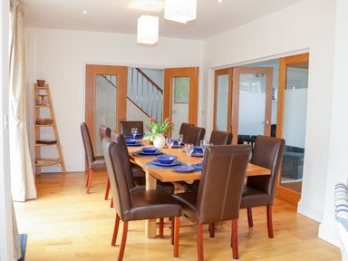 A dining room with a wooden table set with blue dishes and glasses and brown chairs at 1 Orchard Cottages in Salcombe