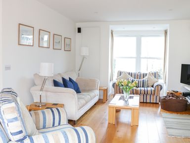 A living room with striped armchairs and sofas a wooden coffee table with flowers and a television at 1 Orchard Cottages in Salcombe