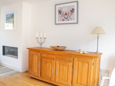 A wooden sideboard with a candle holder a wicker bowl and a lamp in a room at 1 Orchard Cottages in Salcombe