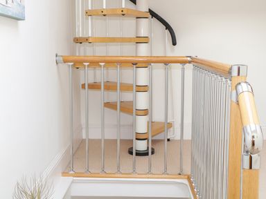 A spiral wooden staircase behind a metal and wooden safety gate at 1 Orchard Cottages in Salcombe