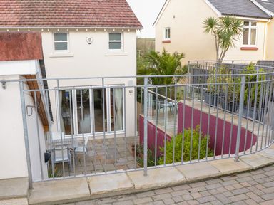 An outdoor patio area with a metal railing and a table with chairs near cream colored buildings at 1 Orchard Cottages in Salcombe