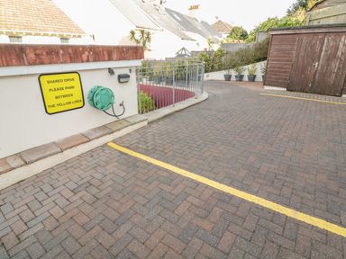 A shared drive with yellow parking lines and a sign on the wall next to a green hose reel near a wooden shed