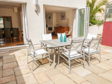 An outdoor patio with a table and six chairs in front of a house with open sliding doors at 1 Orchard Cottages in Salcombe