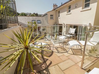 A patio area with white chairs, a glass table with drinks, and potted plants at 1 Orchard Cottages Salcombe