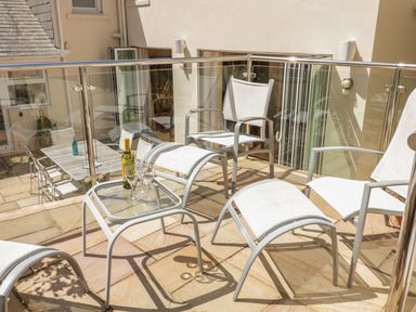 A balcony with white chairs a glass table with wine bottle and glasses at 1 Orchard Cottages in Salcombe