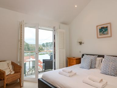 A bedroom with a bed and pillows beside a door opening to a balcony with chairs at 1 Orchard Cottages in Salcombe