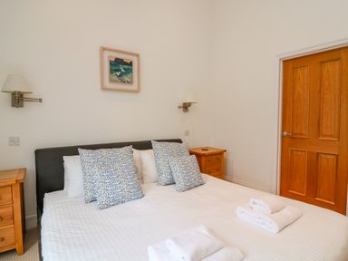 A bedroom with a double bed with patterned pillows two wooden bedside tables wall lamps and a wooden door at 1 Orchard Cottages in Salcombe