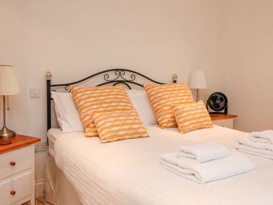 A bedroom with a bed with orange fish patterned pillows white towels on the bed and bedside tables with lamps at 1 Orchard Cottages in Salcombe