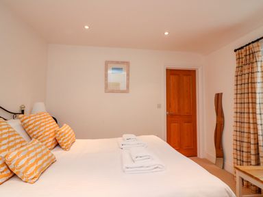 A bedroom with a bed with orange patterned pillows folded towels on the bed a wooden door plaid curtains and a wavy mirror at 1 Orchard Cottages in Salcombe