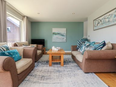 A living room with brown sofas a wooden coffee table and paintings on the walls at Lodge Sixty Six in St Columb Major