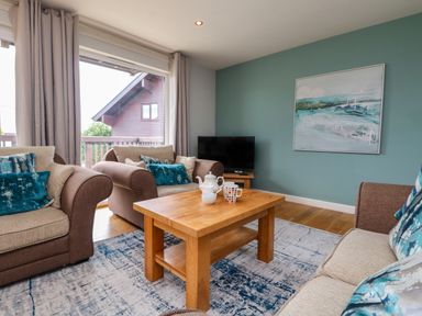 A living room with armchairs cushions wooden coffee table and a television at Lodge Sixty Six in St Columb Major