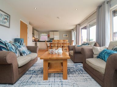 A living room with brown and beige sofas around a wooden coffee table and a dining table with chairs in the background at Lodge Sixty Six in St Columb Major