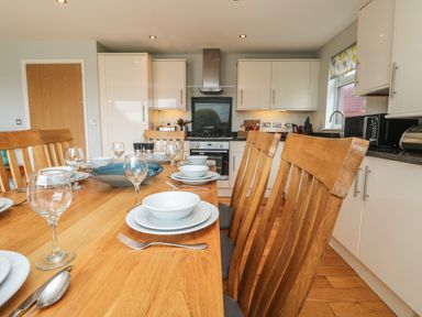 A kitchen dining area with a wooden table set with plates bowls and glasses at Lodge Sixty Six in St Columb Major