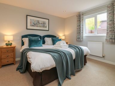A bedroom with a double bed with blue headboards blue pillows and throws bedside tables with lamps and a window with curtains at Lodge Sixty Six in St Columb Major