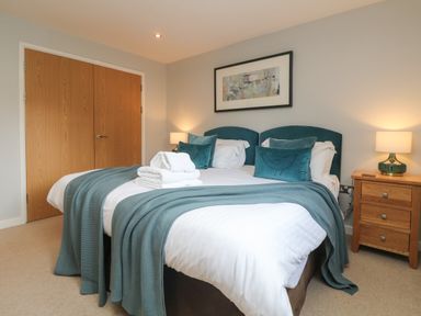 A bedroom with a double bed with blue cushions and blankets bedside tables with lamps and wooden doors at Lodge Sixty Six in St Columb Major