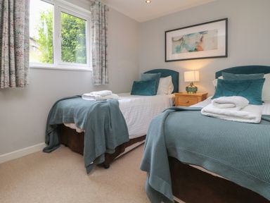 A bedroom with two single beds with teal blankets and pillows a nightstand with a lamp and a framed picture on the wall at Lodge Sixty Six in St Columb Major