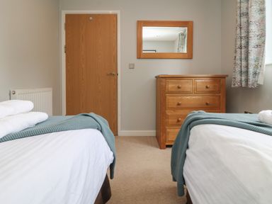 A bedroom with two single beds a wooden chest of drawers a wooden door and a window with curtains at Lodge Sixty Six in St Columb Major
