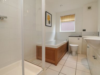 A bathroom with a shower, bathtub, toilet, sink, window with yellow blind and framed artwork at Lodge Sixty Six in St Columb Major