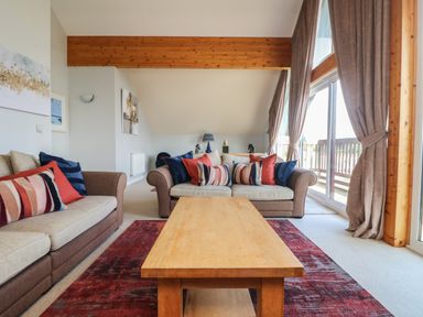 A living room with two sofas around a wooden coffee table and large windows with curtains at Lodge Sixty Six in St Columb Major