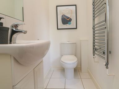 A bathroom with a sink and faucet a toilet a framed picture on the wall and a chrome towel radiator at Lodge Sixty Six in St Columb Major
