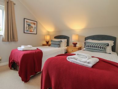 A bedroom with two single beds lamps on wooden bedside tables and folded towels on red blankets at Lodge Sixty Six in St Columb Major