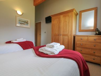 A bedroom with two single beds red blankets white towels wooden wardrobe and dresser with mirror at Lodge Sixty Six in St Columb Major