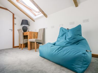 A room with a blue bean bag chair a wooden desk striped chairs and a black lamp under exposed wooden beams at Miner's Rest in Troon near Camborne