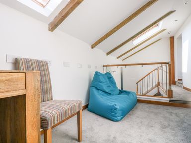 A small seating area with a striped chair and a blue bean bag beside a wooden desk under a ceiling with exposed wooden beams at Miner's Rest in Troon near Camborne