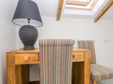 A wooden desk with a black table lamp and two striped chairs under a skylight at Miner's Rest in Troon near Camborne