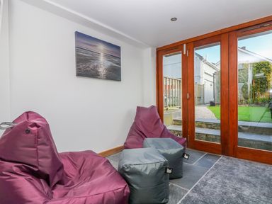 A small seating area with bean bag chairs and ottomans next to glass doors leading to a garden at Miner's Rest in Troon near Camborne