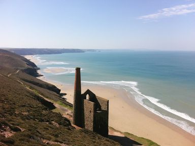 A coastal landscape with an old stone chimney and building ruins overlooking a sandy beach and ocean at Miner's Rest in Troon near Camborne