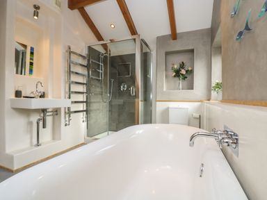 A bathroom with a white bathtub a glass shower enclosure a sink toilet flowers on shelves at Miner's Rest in Troon near Camborne