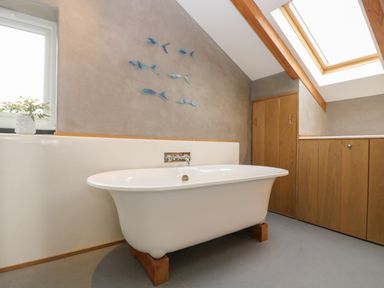 A bathroom with a freestanding bathtub under a slanted ceiling with a skylight at Miner's Rest in Troon near Camborne
