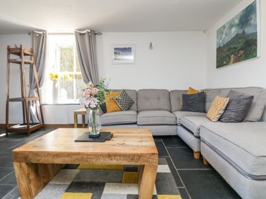 A living room with a gray sectional sofa and wooden coffee table with flowers at Miner's Rest in Troon near Camborne