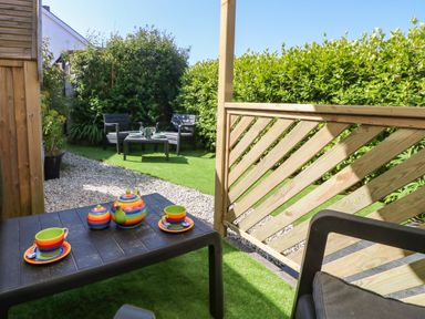 A garden seating area with a black table set with colorful teapot and cups a wooden fence and green hedges at Miner's Rest in Troon near Camborne