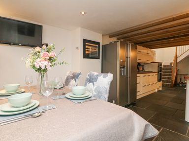 A kitchen and dining area with a table set with plates glasses and a vase of flowers at Miner's Rest in Troon near Camborne