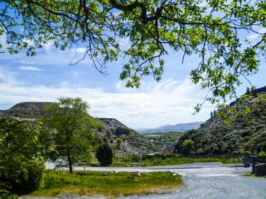A gravel path with green trees and rocky hills under a blue sky at Stiniog Lodge in Blaenau Ffestiniog