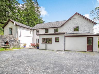 Exterior view of a white stone house with multiple windows and a gravel driveway at Stiniog Lodge in Blaenau Ffestiniog