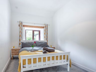 A bedroom with a white bed frame yellow blanket and window with patterned curtains at Stiniog Lodge in Blaenau Ffestiniog