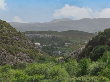 A landscape with green trees rocky hills and houses in the distance at Stiniog Lodge in Blaenau Ffestiniog