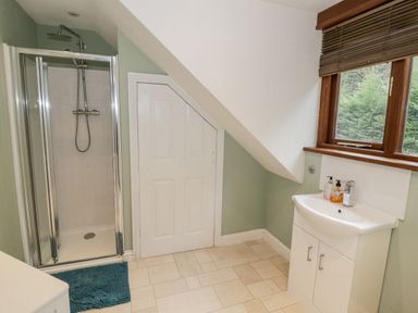 A bathroom with a shower, sink with cabinet, a window with blinds and a door under a slanted ceiling at Shatterford Lakes in Shatterford