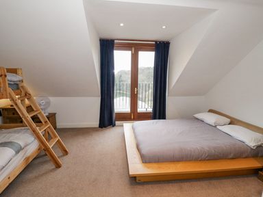 A bedroom with a double bed with pillows a wooden bunk bed a wooden nightstand with a fan and glass doors with dark curtains at Shatterford Lakes in Shatterford