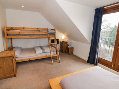 A bedroom with a bunk bed a small wooden chest of drawers a lamp and a fan next to a window with blue curtains at Shatterford Lakes in Shatterford