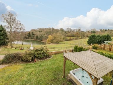 A garden with a wooden gazebo and hot tub overlooking a pond and trees at Shatterford Lakes in Shatterford