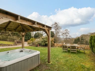 An outdoor space with a covered hot tub and a wooden table with six chairs on grass at Shatterford Lakes in Shatterford