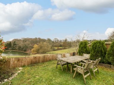 A garden with wooden table and chairs near a wooden fence overlooking a lake and trees at Shatterford Lakes in Shatterford