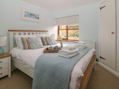 A bedroom with a double bed with cushions and folded towels a nightstand window with blinds and a built in closet at Erin Cottage in Pelynt near Looe